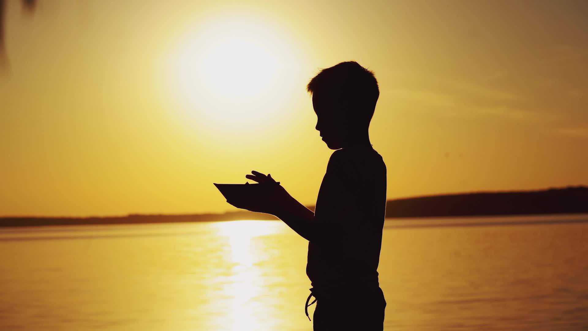 小男孩在夕阳下的湖边折纸船